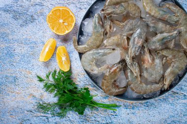 Taze çiğ karides, limon ve mermer bir yüzeyde kişniş dilimleri ile buza yayılmış, pişirmeye hazır, insan yok.