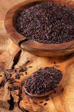 Tahta bir kâse içinde doğal siyah pirinç ve tahta bir yüzey üzerinde kırsal tarzda kaşık.