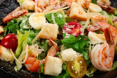 Kaplan karidesli sezar salatası, karides salatası, marul yaprağı, bıldırcın yumurtası, vişneli domates, parmesan peyniri, siyah tabakta.,
