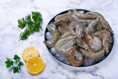 Taze çiğ karides, limon ve mermer bir yüzeyde kişniş dilimleri ile buza yayılmış, pişirmeye hazır, insan yok.