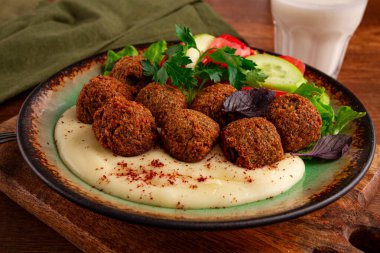 Bir tabakta falafel topları, tahini, domatesli salata ve salatalık ve bir içki var. Ortam sıcak ve davetkar. Taze malzemelerle öğle yemeği için mükemmel..