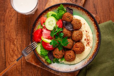 Bir tabakta falafel topları, tahini, domatesli salata ve salatalık ve bir içki var. Ortam sıcak ve davetkar. Taze malzemelerle öğle yemeği için mükemmel..