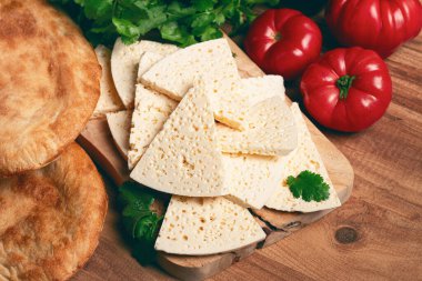 Gürcistan usulü dilimlenmiş peynir, ahşap bir doğrama tahtasında, domatesli otlar ve lavaşla, kırsal tarzda, Gürcü mutfağı, insan yok.