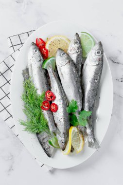Taze ringa balığı, pişirmeye hazır, otlar ve baharatlarla, beyaz bir tabakta, mutfakta.