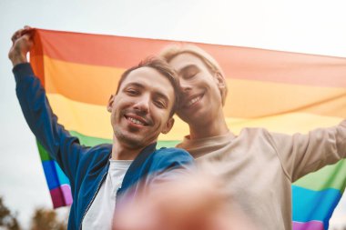 Romantik eşcinsel çift dışarıda sarılıyor, öpüşüyor ve el ele tutuşuyor. İki yakışıklı adam selfie çekerken LGBT gurur bayrağı taşıyor..