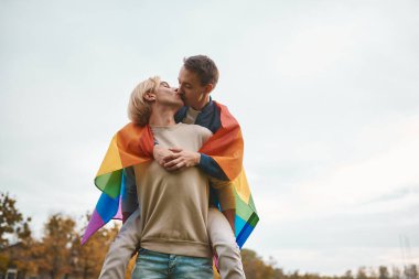Romantik eşcinsel çift dışarıda sarılıyor, öpüşüyor ve el ele tutuşuyor. LGBT gurur bayrağı taşıyan iki yakışıklı adam..
