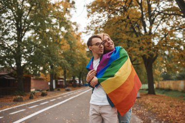 Romantik eşcinsel çift dışarıda sarılıyor, öpüşüyor ve el ele tutuşuyor. Parkta LGBT gurur bayrağı taşıyan iki yakışıklı adam..