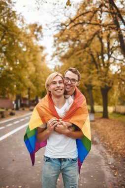 Romantik eşcinsel çift dışarıda sarılıyor, öpüşüyor ve el ele tutuşuyor. Parkta LGBT gurur bayrağı taşıyan iki yakışıklı adam..