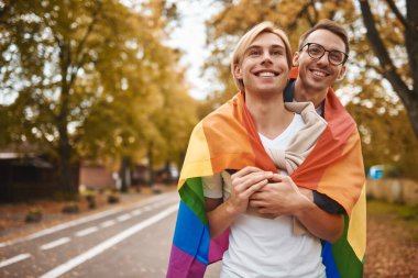 Romantik eşcinsel çift dışarıda sarılıyor, öpüşüyor ve el ele tutuşuyor. Parkta LGBT gurur bayrağı taşıyan iki yakışıklı adam..