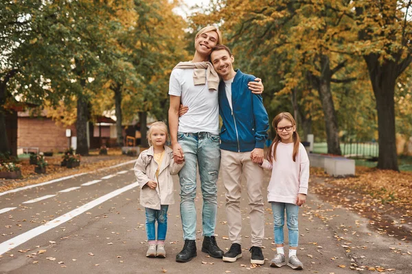 Two gay parents with their adopted daughters walking in park together. Happy LGBT family concept.
