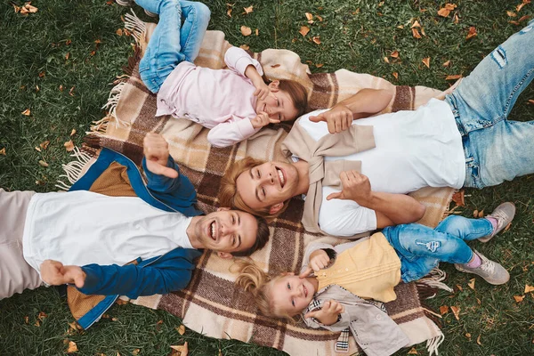 Two gay parents with their adopted daughters having fun together while lying on blanket in park. Happy LGBT family concept.