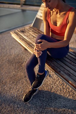 Diz kapağı ağrısı, koşudan sonra kramp. Dayanıksız sporcu kız. Kadın diz kapağına tutunuyor. Spor sakatlığı. Sağlıklı yaşam tarzı kavramı. Bir sabah koşusundan sonra yaralanma