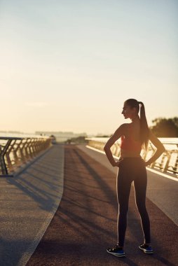 Güzel kız gün doğumunda spor yapıyor ve poz veriyor. Genç bir kadının bakış açısı. Şehirde spor haberleri. Şehir konseptinde sağlıklı yaşam tarzı. Sabahları koşuyorum.