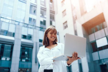 Şehirde genç ve çekici bir iş kadını. Bilgisayarla modern iş merkezinin yanında yürüyorum..