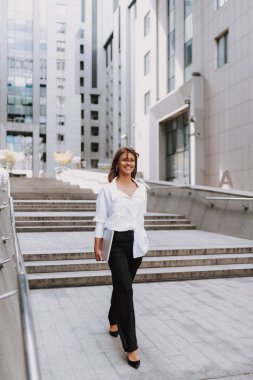 Şehirde genç ve çekici bir iş kadını. Bilgisayarla modern iş merkezinin yanında yürüyorum..