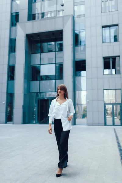 Young attractive business woman in the city. Walking near modern business center with laptop.