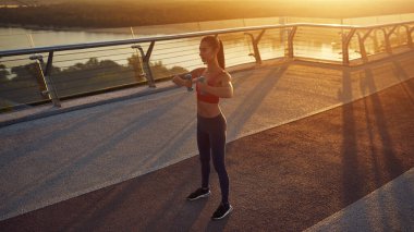 Dambıllarla sabah egzersizleri, karantina koşullarında. Sağlıklı yaşam tarzı kavramı. Gün doğumunda dambıllarla egzersiz. Güneş kameraya doğru parlıyor.