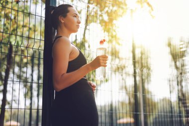 Siyah spor giysili genç bir kadın parkta esniyor ve spor yapıyor. Molada su içen çekici fit bir kız. Sağlıklı yaşam tarzı kavramı.