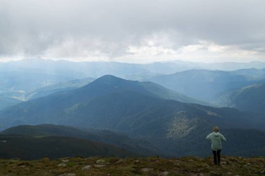Yeşil kazaklı bir kız, tırmandıktan sonra bulutlardaki dağların güzel manzarasına hayran kalır.