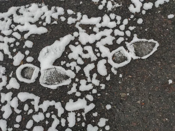 Prachtig smeltende sneeuw rond voetafdrukken op het asfalt. Rechtenvrije Stockafbeeldingen