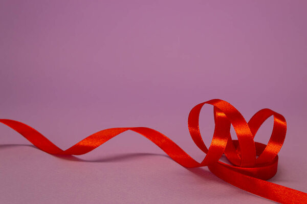 Red satin ribbon curls on a lilac background, free space.