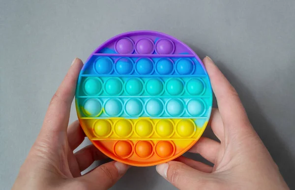 Heldere kleurrijke siliconen Pop it toy. Populaire anti-stress speelgoed op een grijze achtergrond in de handen van een vrouw Rechtenvrije Stockafbeeldingen