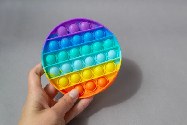 Bright colorful silicone Pop it toy. Popular anti-stress toy on a gray background in the hands of a woman