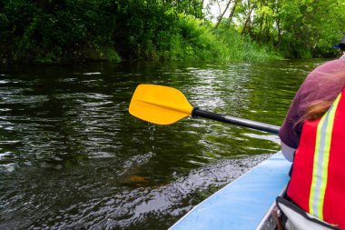 Nehirde kano yaparken bir kızın ellerinde sarı kürek çekmek için bir kürek