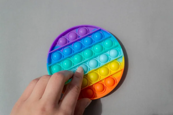 Φωτεινό πολύχρωμο σιλικόνη Pop αυτό παιχνίδι. Δημοφιλή αντι-στρες παιχνίδι σε γκρι φόντο, ένα γυναικείο χέρι πιέζει τις φυσαλίδες — Φωτογραφία Αρχείου