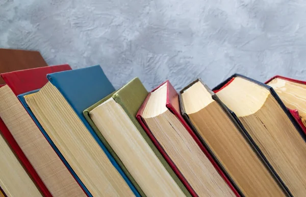 Řada pestrobarevných padajících knih na dřevěném stole na šedé a modré betonové stěně — Stock fotografie