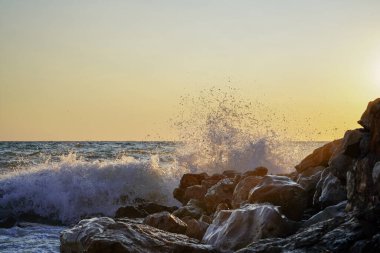 Denizde gün batımı. Kaya kıyısı, su sıçrıyor. Dalgalar kıyıya çarpıyor. Plaj kayasında deniz dalgası kırılıyor. Deniz dalgaları çarpar ve kayalara çarpar. Deniz manzarası, okyanus.
