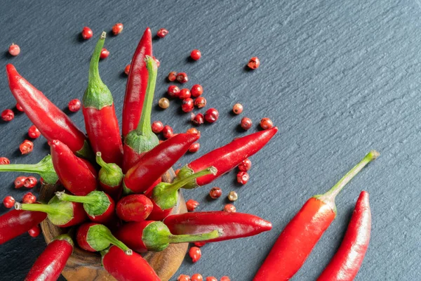 A bunch of red hot chili peppers in a wooden stand. Cayenne peppers and red peppercorns on a black granite background.