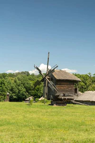 Antiguo molino de viento y casas rurales tradicionales ucranianas medievales en un prado verde. Cielo azul con nubes blancas. —  Fotos de Stock