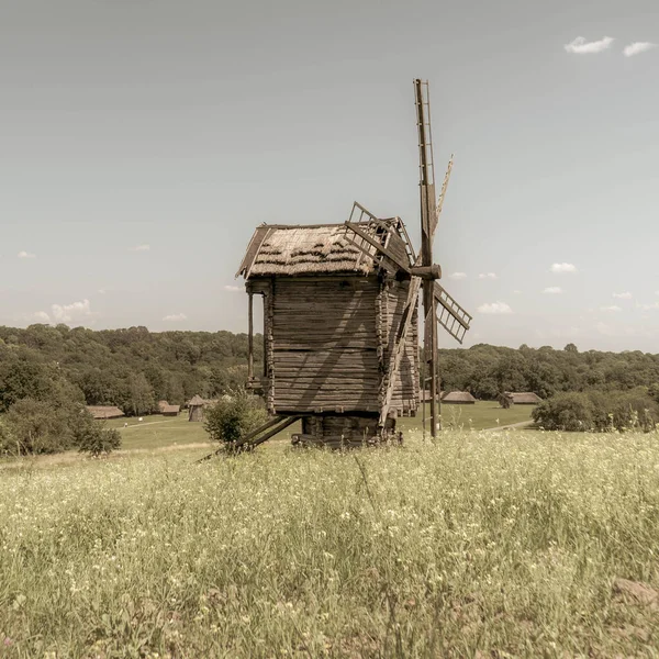 Antiguo molino de viento y casas rurales tradicionales ucranianas medievales en un prado verde. Cielo azul con nubes blancas. Foto vieja. — Foto de Stock