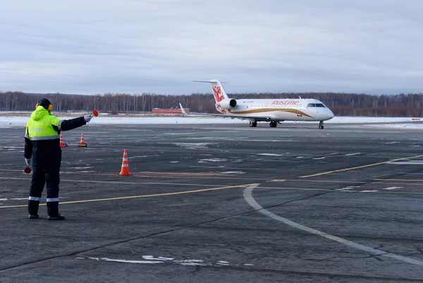 Nischni nowgorod. Russland. 26. januar 2015. der mitarbeiter des flughafens mann weist den piloten des bombardier crj 100 flugzeugs der russischen fluglinie auf einen parkplatz hin — Stockfoto