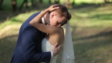 Gelin ve damat sarılma, öpüşme ve parkta düğün gününde gülümseyen.