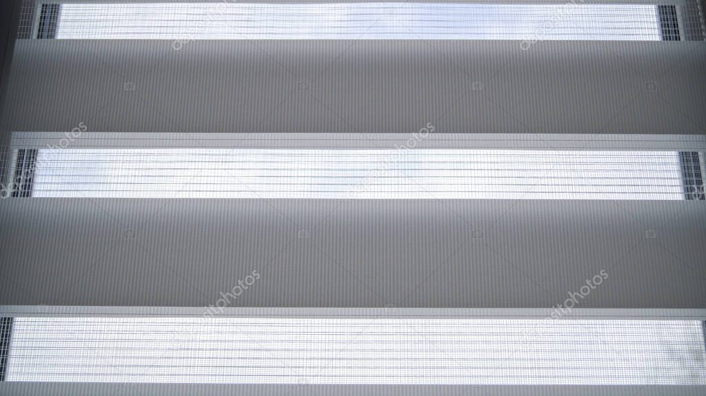 White roller blinds with stripes and mesh on a plastic window in the room. Day and night system. It's a nasty day. Comfort and refinement of the house.