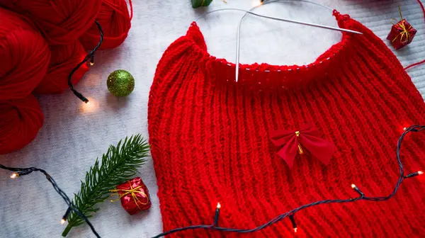 Lavorare un maglione rosso di Natale sullo sfondo dell'arredamento di Capodanno con una ghirlanda. Mi preparo a festeggiare Natale e Capodanno. Lavorare a mano. Palle di lana con filo rosso. Fatto a mano. — Foto Stock