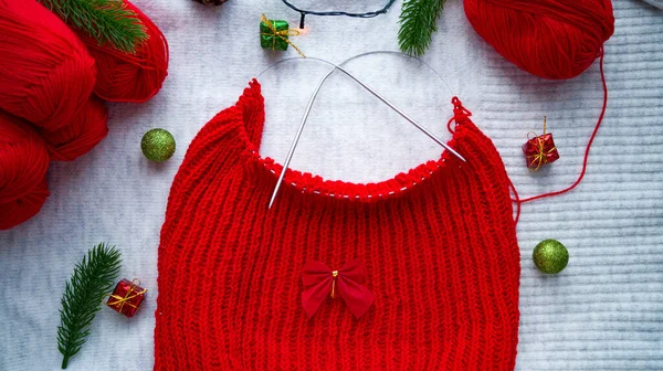 Knitting red Christmas sweaters on the background of New Years decor. Preparing to celebrate Christmas and New Year. Knitting by hand. Woolen balls of red thread. Handmade.