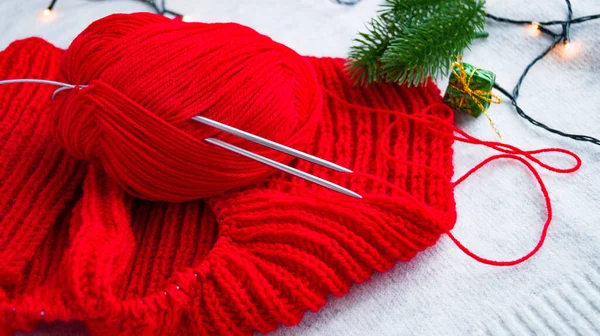 뜨개질 바늘은 새 년 10 월에 작은 배경에 있는 빨간 제품 뭉치에 박혀 있다. 크리스마스 스웨터를 혼자 뜨개질하는 거. 새해와 크리스마스를 축하 할 준비를 하는 모습. — 스톡 사진