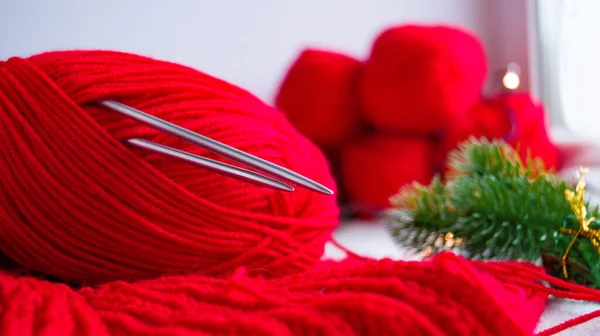 Stricknadeln stecken in einem Knäuel roter Produkte im Silvesterdekor auf hellem Hintergrund. Selbstgestrickter Weihnachtspullover. Vorbereitung auf das neue Jahr und Weihnachten. — Stockfoto