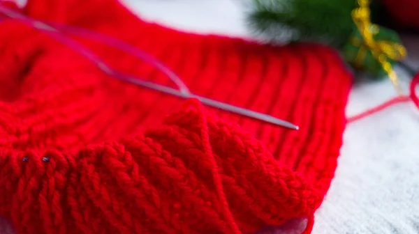 Deel van een gebreid rood product op een lichte achtergrond in kerstdecor. Engelse kauwgom. Handbreien. Breien van een warme trui voor herfst en winter. Voorbereiding om het nieuwe jaar en de kerst te vieren. — Stockfoto