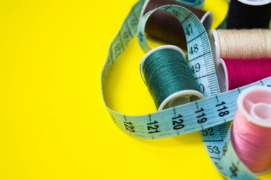 Bir santimetre ve çok renkli iplik makaraları sarı arka plana saçılmıştır. Dikiş, dikiş, nakış için malzeme ve aksesuar. Metnin için yer.