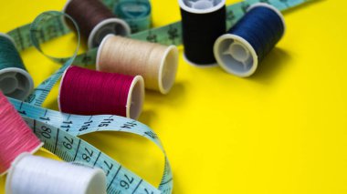 Bir santimetre ve çok renkli iplik makaraları sarı arka plana saçılmıştır. Dikiş, dikiş, nakış için malzeme ve aksesuar. Metnin için yer.