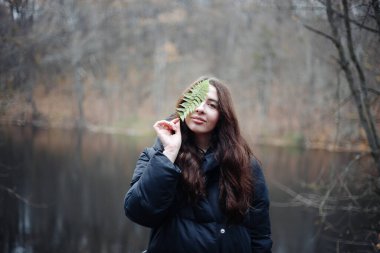 Genç bir kadın eğreltiotu yaprağıyla yüzünü kapatıyor.