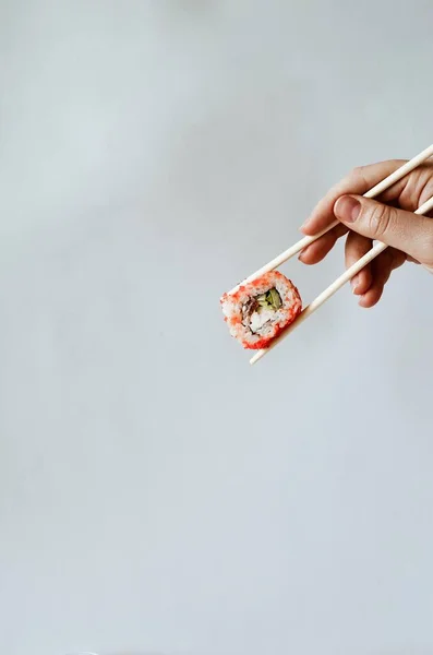 Mâna unei tinere care ține bețe de sushi și o rola Philadelphia — Fotografie, imagine de stoc