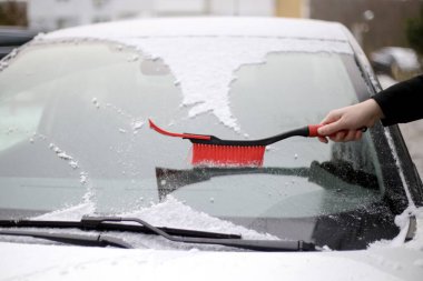 Bir adam kırmızı bir fırçayla arabanın ön camından karı temizler.