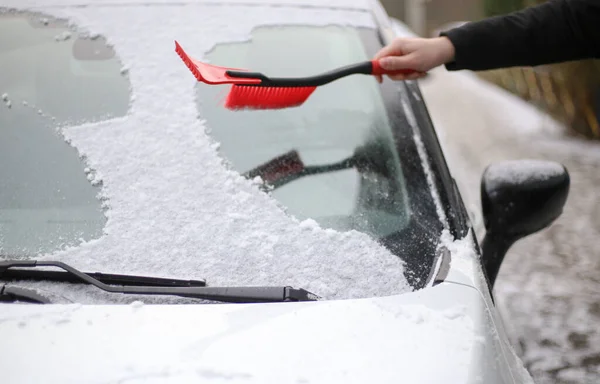 Um homem limpa a neve do pára-brisas de um carro com uma escova vermelha — Fotografia de Stock