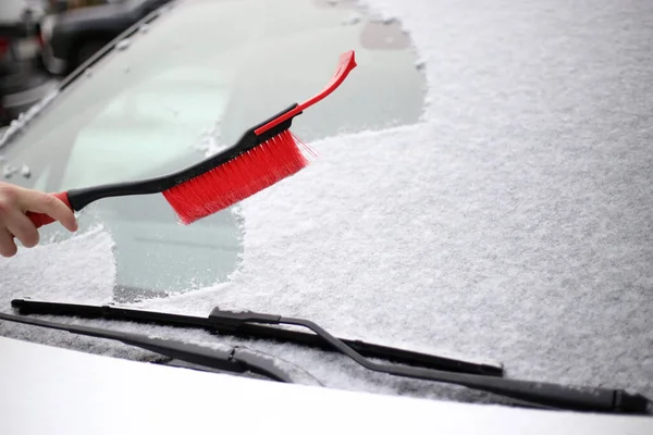 A man cleans snow from the windshield of a car with a red brush — Stock Photo, Image
