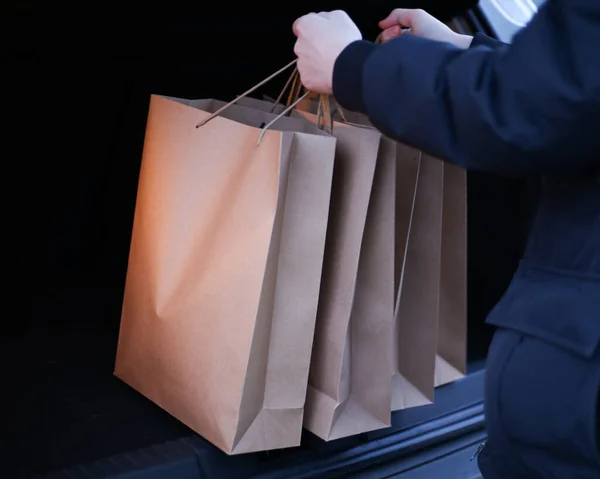 Un jeune homme met des sacs à provisions en papier dans le coffre d'une voiture — Photo